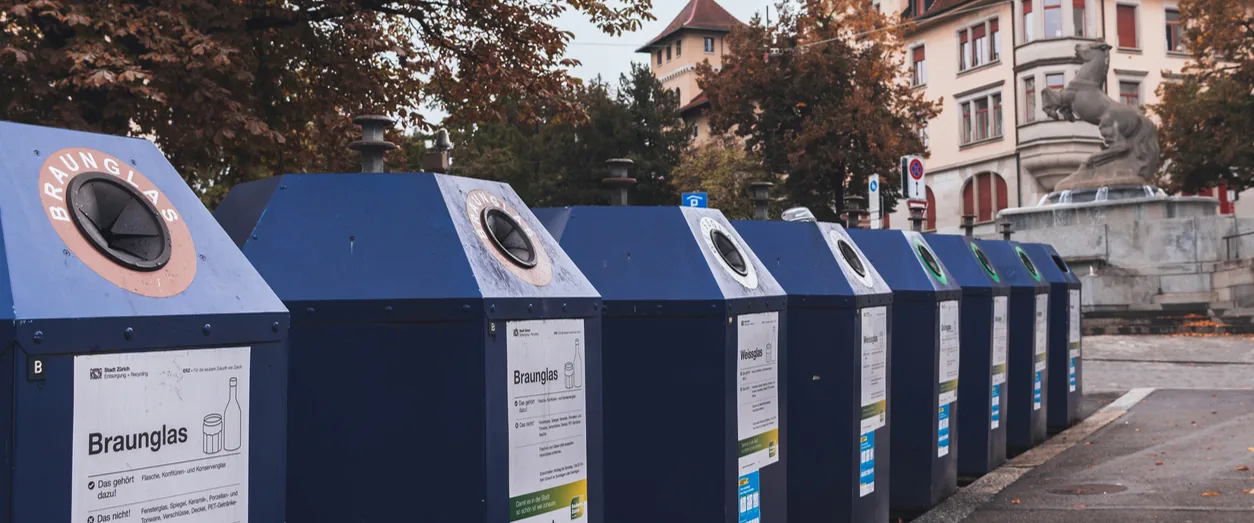 Contenedores azules de recogida selectiva de vidrio con señalización en alemán en un entorno urbano suizo