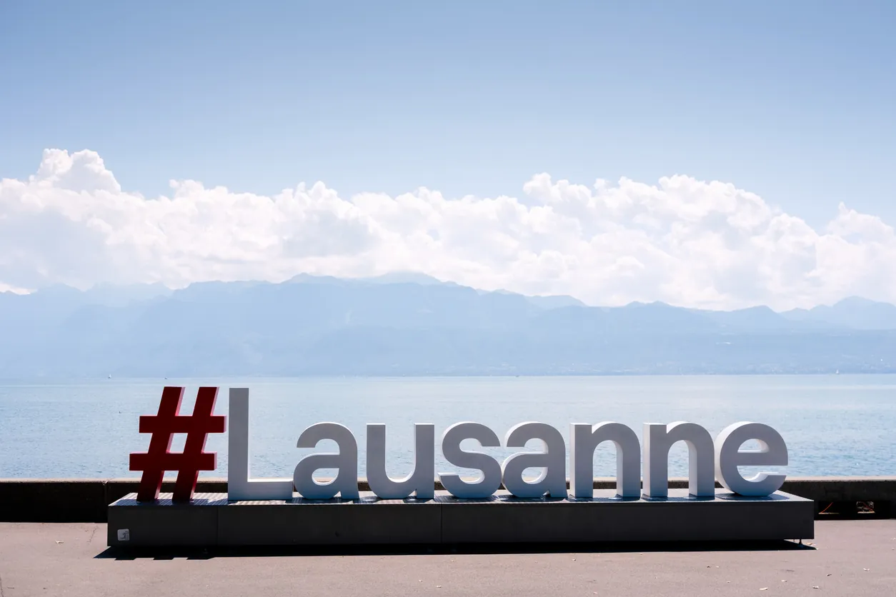 Letrero de Lausanne junto al lago Lemán con montañas al fondo